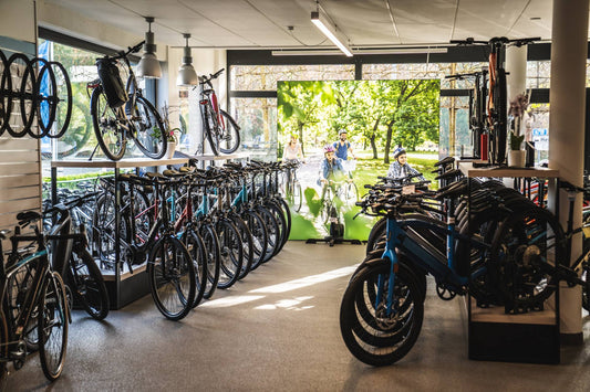 Interior view of a bike shop featuring various city and e-bikes, with a large display panel in the background showing a family cycling in a sunny park.