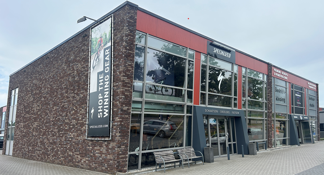 A modern two-story Specialized store with large windows, a banner showing a cyclist, and a bicycle displayed inside.