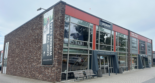 A modern two-story Specialized store with large windows, a banner showing a cyclist, and a bicycle displayed inside.