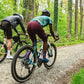 Two cyclist riding gravel through a forest